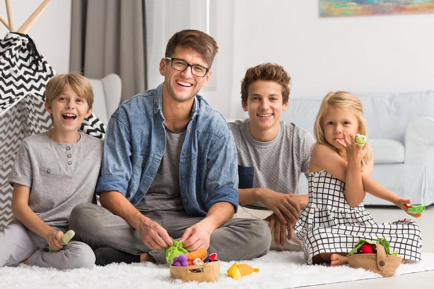 Father and three children playing with Montessori-style felt toys on a rug at home
