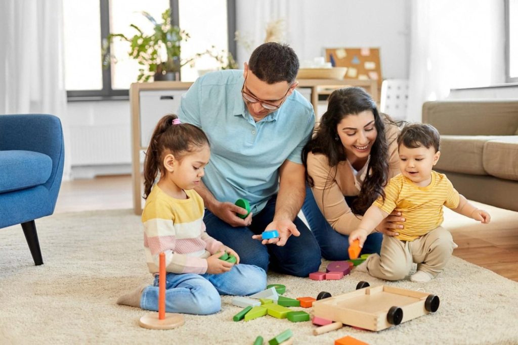 Parents helping two children play with wooden Montessori shape sorters and blocks